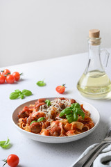 Pasta fettuccine with meatballs, parmesan, tomatoes, basil on white table. Close up. Vertical format.