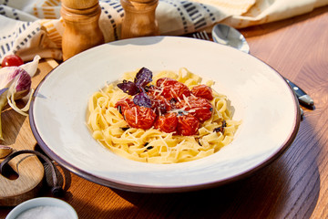 delicious pasta with tomatoes, parmesan and red basil served on wooden table in sunlight