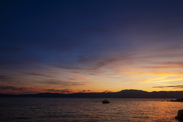 Silhouette of lonely boat in the sunset with dramatic sky. High seas sunset with a fishing ship on the horizon.