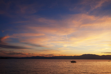 Silhouette of lonely boat in the sunset with dramatic sky. High seas sunset with a fishing ship on the horizon.