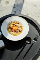 delicious pasta carbonara served with cutlery on black table on marble background in sunlight