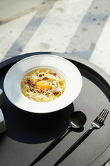 delicious pasta carbonara served with cutlery on black table on marble background in sunlight