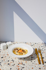 delicious pasta carbonara served with golden cutlery, salt and pepper shakers on stone table in sunlight