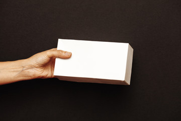 Women's hands hold A white rectangular box on a dark background