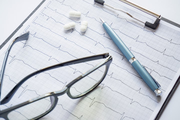 cardiogram with stethoscope, pen, magnifier, pills and glasses lay on a table