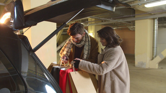 A woman opens the trunk, a man puts packages in the car