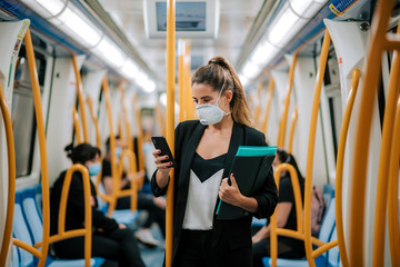 young woman with medical mask in the subway uses her phone