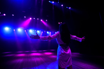 Obraz premium Unrecognizable singer standing on stage at microphone, back view, neon lights