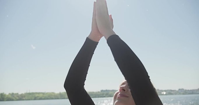 Young Blonde Woman practicing yoga on the wooden berth at lake. Single sport healthy training on nature at sunny weather