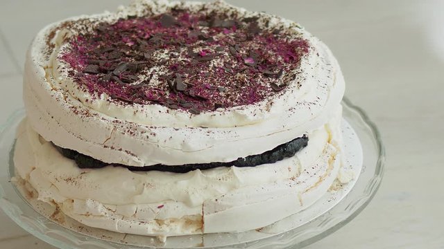 Kid tase delicious Meringue Cake from a plate by finger. Decorated with chocolate and forrest fruits