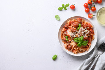 Pasta fettuccine with meatballs, parmesan, cherry tomatoes, basil on white table. View from above. Space for text.