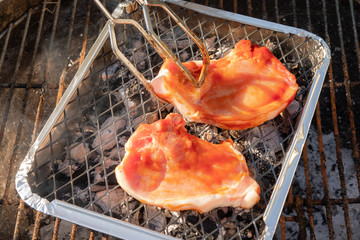 Freshly prepared pork chops in marinated sauce seen being laid on a disposable barbecue.
