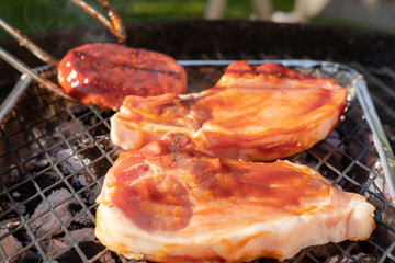 Fresh chops and a burger seen being placed on a disposable BBQ in an outdoor location. The meats...