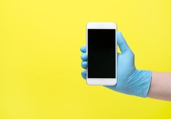 yellow background and hand in medical glove. Male hand in latex medical blue glove shows mobile phone screen