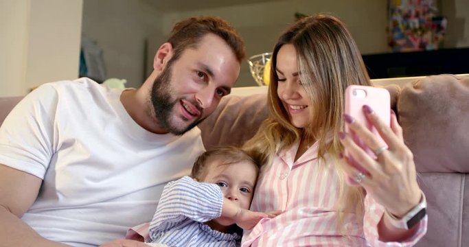 married couple and their little daughter are filming themselves by smartphone at home