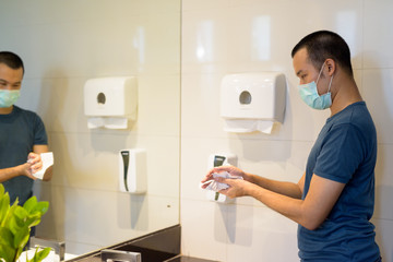 Young Asian man wearing mask and drying hands properly with tissue in the bathroom