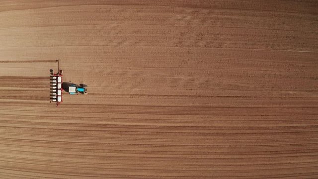 Aerial view of tractor with mounted seeder performing direct seeding of crops on plowed agricultural field. Farmer is using farming machinery for planting process, top view