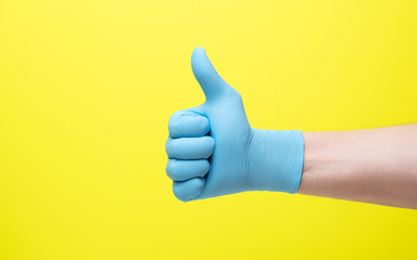 yellow background and hand in medical gloves.male hand in latex medical blue glove shows good luck gesture