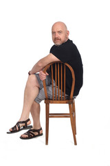 Bald man with sandals t-shirt and shorts sitting on white background, looking at camera and chair back