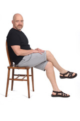Bald man with sandals t-shirt and shorts sitting on white background, looking at camera