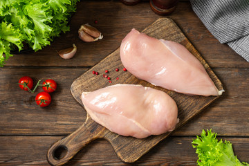 Chicken breast fillet on a wooden Board on a brown wooden table. Raw chicken breast. Top view  - obrazy, fototapety, plakaty