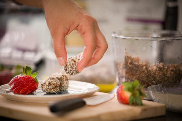 Plate with delicious homemade protein balls in the girl's hand and ripe strawberries. Healthy sweets. Organic raw treats from nuts, coconut, dates and cocoa