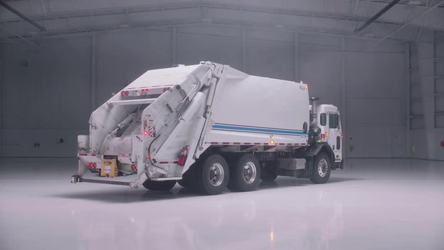 Push in on a white, clean garbage truck in an empty warehouse.
