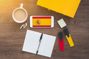 flag and coat of arms of spain, smartphone, wireless headphones, spanish textbook, notepad on a...