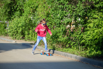 Little Girl in jeans and sunglasses rides a skateboard around the yard