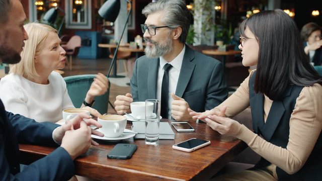 Businessmen and businesswomen in formalwear are speaking in cafe discussing work gesturing sitting at table together. People and restaurant concept.