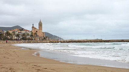 A beautiful beach in Sitges, near Barcelona. Light waves roll onto Spain's Mediterranean beach. Beautiful architecture of Catalonia. Unique landscapes of the Iberian Peninsula