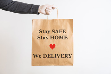 Naklejka na ściany i meble Concept of shipment of product of take away and advertising in virus quarantine from Coronavirus, Covid-19 - Hand of a man holding paper bag written Stay Safe Stay Home We delivery with heart symbol