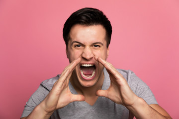 Hear me roar! Close-up shot of a young man in casual clothes, who is screaming while holding his arms near his mouth.