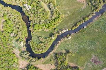 Aerial top down view of Ukrainian plain river Psel during spring time. Beautiful valley of riverbed rounded by green meadows of grass and willow trees. Beauty of summer nature. River delta from above.