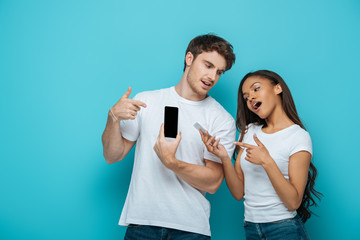 attractive african american girl with handsome boyfriend pointing with fingers at smartphones on blue background