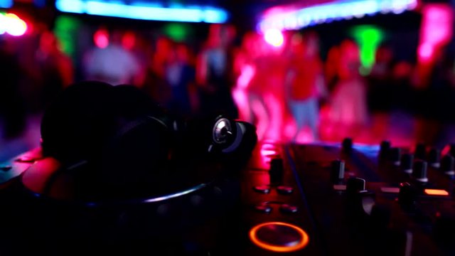 DJ music control panel with headphones on the background of dancing people in a nightclub, copy space