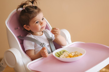 Obraz na płótnie Canvas Portrait of happy young baby girl in high chair eating exotic fruits