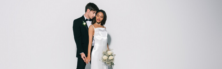 horizontal image of elegant interracial newlyweds standing with closed eyes on white background