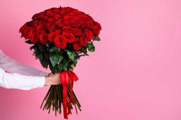 Photo of cropped man arms hold big one hundred red bright roses bunch giving girlfriend surprise hiding face secret admirer arrangement delivery concept isolated over pink color background