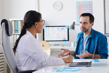 Fototapeta premium Mature man sitting opposite his doctor and telling about his complaints on the health at hospital