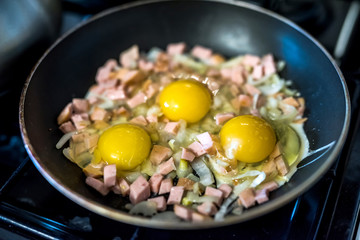 fried egg topped pieces of sausages and onion in hot pan