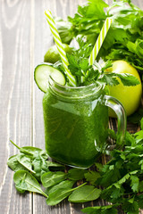 Blended green smoothie with ingredients on wooden table
