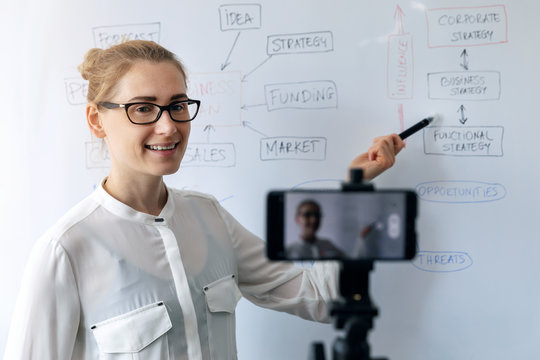 online education, webinar and business vlog concept - woman teaching and recording video with phone in front of whiteboard