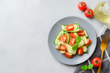 Healthy vegetable salad of fresh cherry tomatoes, cucumbers on a plate. Vegan food. Summer refreshing detox salad. Light gray stone table. Top view, copy space