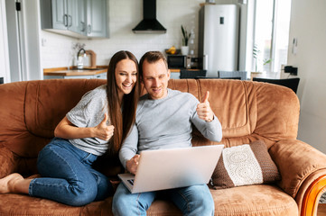 Married couple are at home communicating online via video call, they are sitting on a sofa and using laptop for connect with a family on the distance