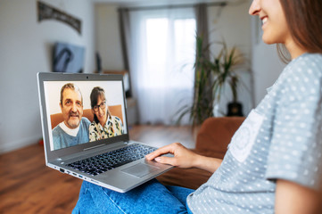 Video call to a parents. A girl is sitting on a couch with a laptop and talking with her parents online. Meeting with a family online