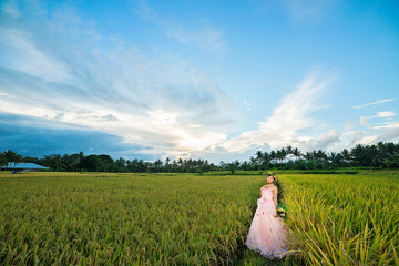 Fototapeta na wymiar 田園のなかにいるピンクのドレス姿の女性