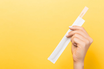 Woman's hand holding chopsticks in a pack on yellow background. Chinese food concept with empty space for your design