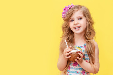 A cheerful little blonde girl drinks a coconut cocktail. A child in a swimsuit with a flower in her hair, summer vacation on the kunikulah. 