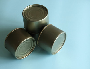 Three tin cans lie on a light blue background and cast a shadow. Canned food, recent food supplies, money running out. Help, family support, canned food in banks